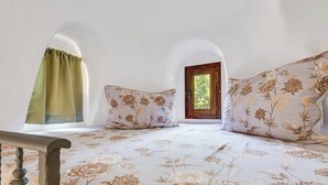 A bedroom with a floral bedspread, a window with a green curtain, and a wooden door leading outside. - Little Castle by Interhome (Skradin)