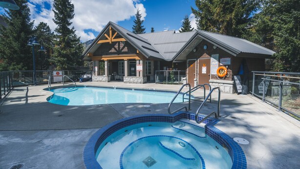 A pool area with a hot tub, a wooden building, and a sign indicating the pool is closed. - Whistler Village Townhome (Whistler)