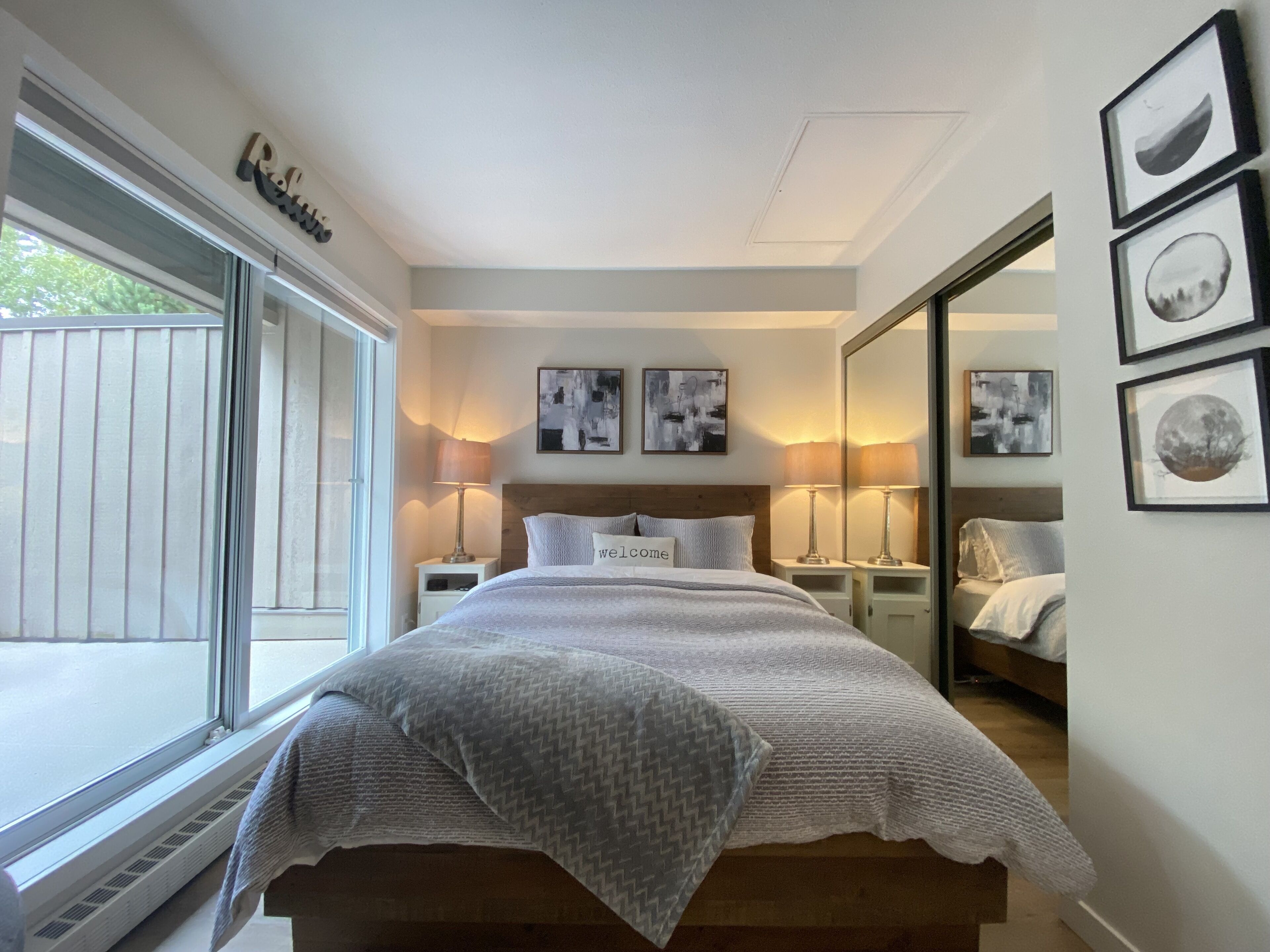 Une chambre à coucher avec un grand lit, des tables de chevet, une fenêtre et des œuvres d’art accrochées aux murs.