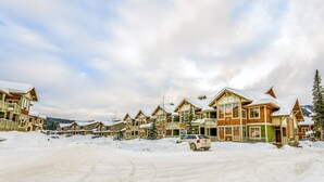Eine Reihe von blockhausartigen Gebäuden mit schneebedeckten Dächern, ein Parkplatz und eine gebirgige Kulisse.