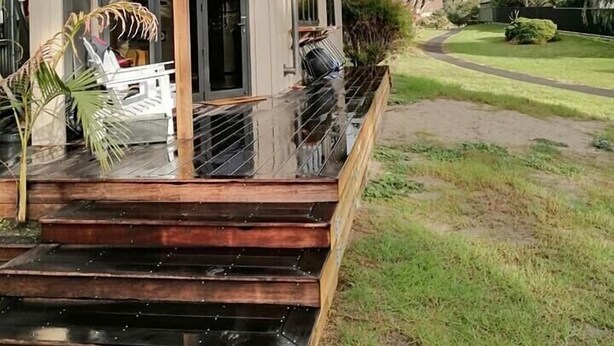 A modern house with a wooden deck and a glass railing, a visible door, and a garden with a curved path. - The Pirate's Rest, a tiny home by the beach. (Pauanui)