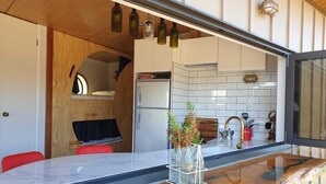 A compact kitchen with a built-in refrigerator, a wooden dining area, and a bar counter with a glass top. - The Pirate's Rest, a tiny home by the beach. (Pauanui)