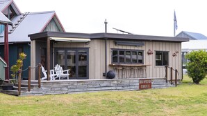 A small, single-story building with a covered patio area, a sign indicating it is a restaurant, and a flagpole with a flag. - The Pirate's Rest, a tiny home by the beach. (Pauanui)