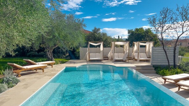 Una piscina rectangular con agua cristalina y azul, rodeada de sillas de descanso y una pérgola.