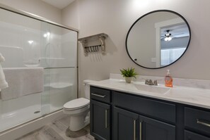 A modern bathroom with a glass shower enclosure, a white toilet, dark cabinets, a round mirror, and a small potted plant on the vanity. - Journey's Remedy (Branson)