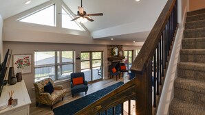 A spacious living area with a high ceiling, a wooden staircase, and a view of the outdoors through large windows. - Journey's Remedy (Branson)