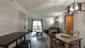 En moderne stue med et træspisebord, en sofa og et stort vindue med gardiner.