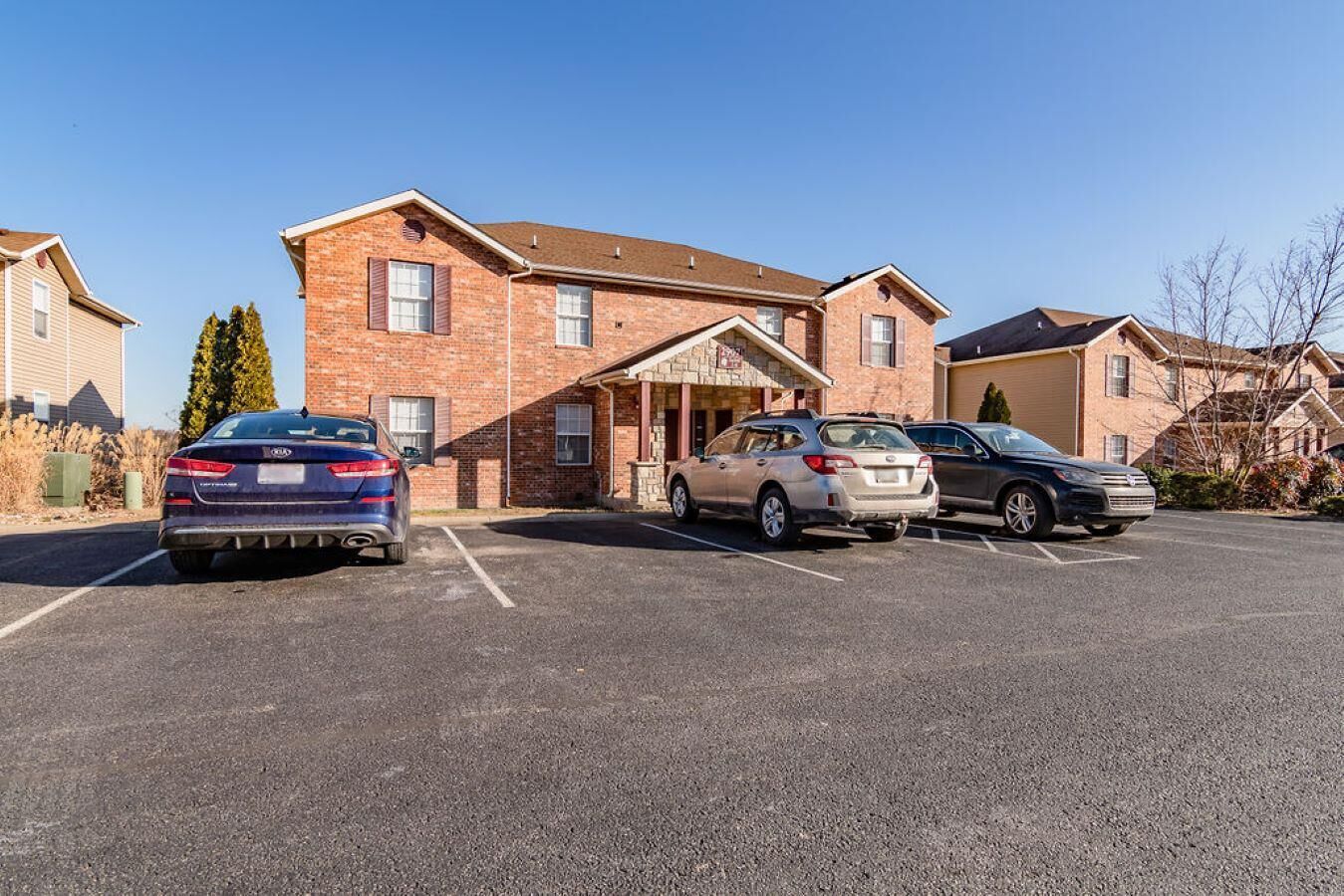 A parking lot with three cars parked in front of a brick building with a covered entrance.