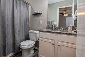 A bathroom with a toilet, a shower curtain, a sink with a mirror, and a ceiling fan. - Spruce Valley (Branson)