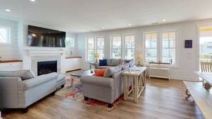 A spacious living room with a fireplace, a large sofa, and a dining area with a table and chairs. - Modern Coastal Retreat w/ Elevator, Large Deck, Water View, Dog Friendly & Big Fenced Yard (Carolina Beach)