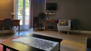 A living room with a large window, a flat-screen TV, a small table, and two chairs. - Appartement Historique (Bagnères-de-Luchon)