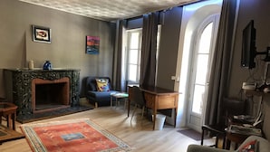 A living room with a fireplace, a sofa, a chair, and a small table. - Appartement Historique (Bagnères-de-Luchon)