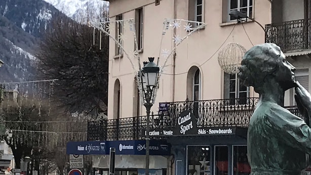 A building with a balcony, a statue, and a mountain backdrop. - Appartement Historique (Bagnères-de-Luchon)