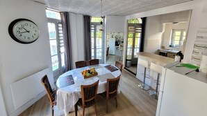 A dining area with a round table, chairs, a clock, and a view of a kitchen and balcony. - Appartement Historique (Bagnères-de-Luchon)