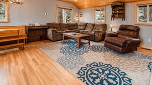 Una sala de estar acogedora con techo de madera, un sofá de cuero marrón, una mesa de centro de madera y una alfombra estampada.