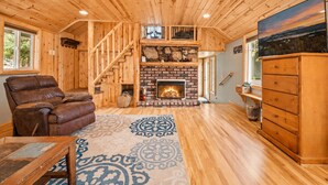 Un interior de madera con chimenea, sofá de cuero y alfombra estampada.