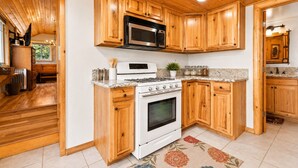 Una cocina con armarios de madera, estufa, microondas y una encimera con frascos.