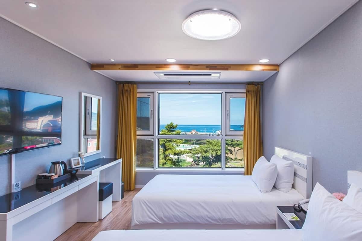 A hotel room with a bed, a desk, a TV, and a window with a view of the sea.