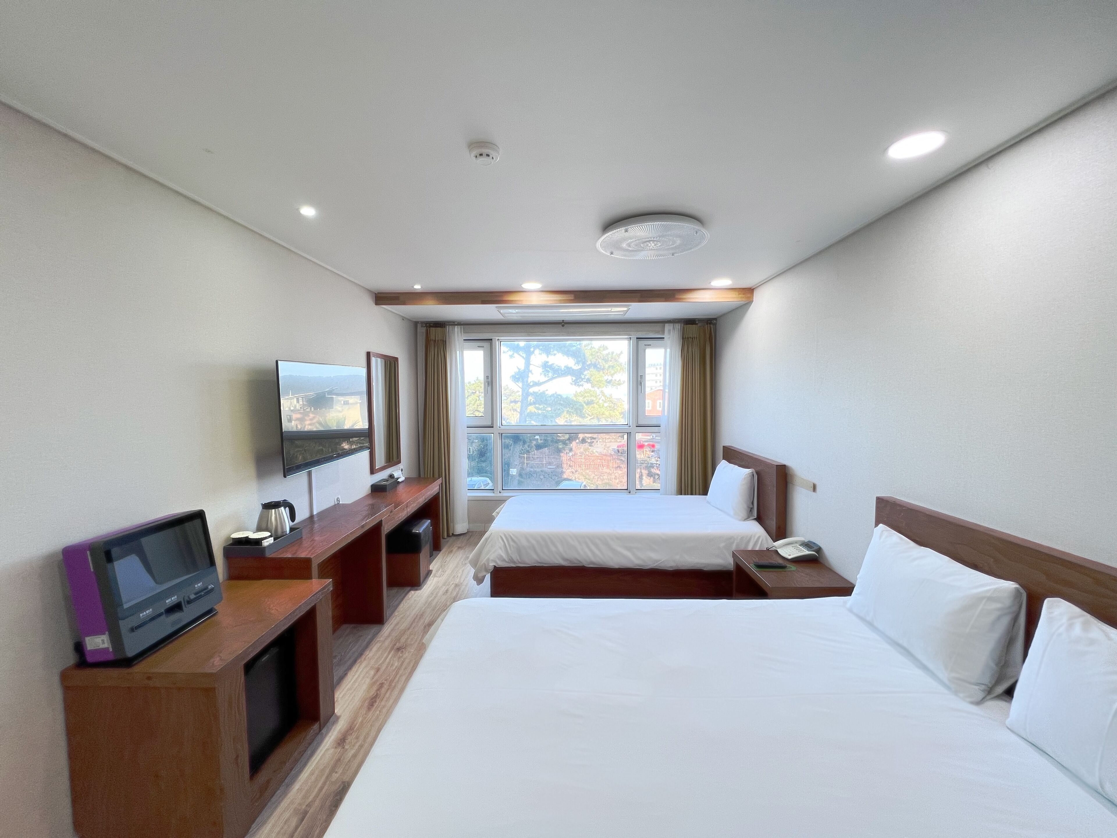 Une chambre d’hôtel avec deux lits, une télévision, un bureau avec un ordinateur et une fenêtre donnant sur des immeubles et des arbres.
