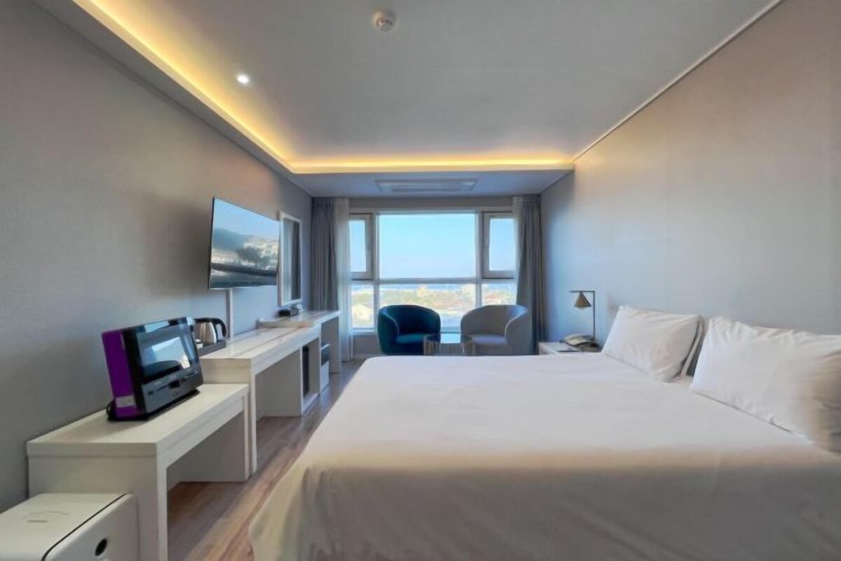 Ein Hotelzimmer mit Bett, Schreibtisch mit Computer, Stuhl, Fernseher und Fenster mit Aussicht.