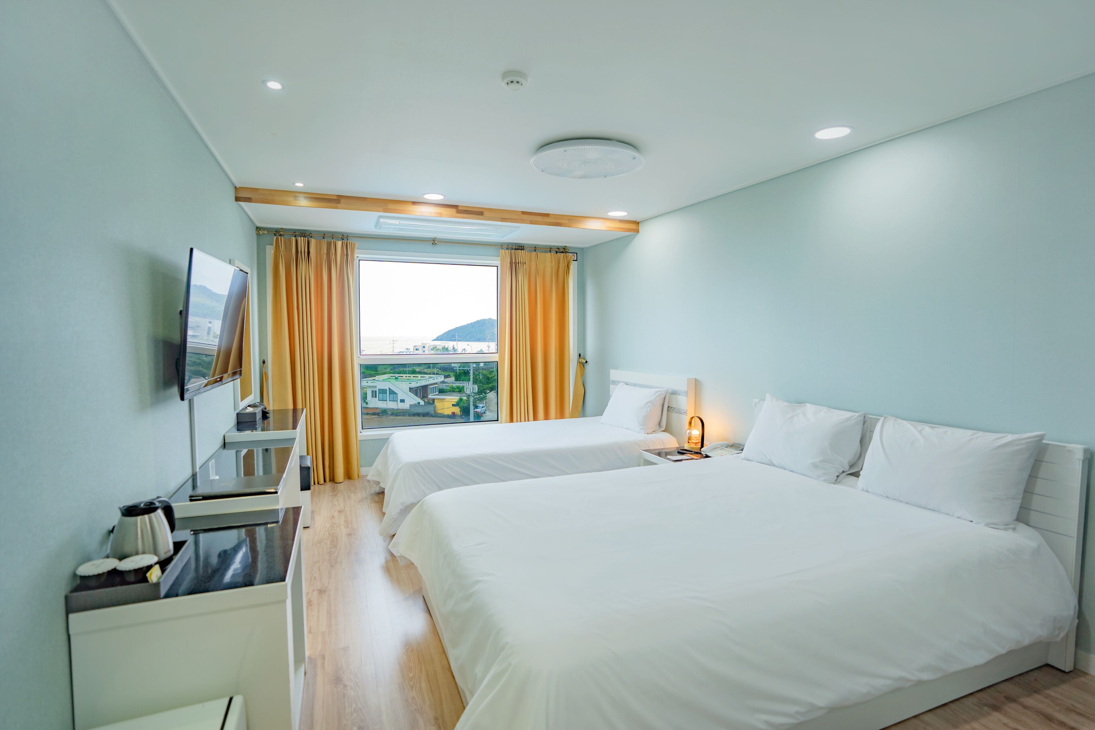 Habitación de hotel con dos camas, un escritorio con hervidor, televisión y ventana con cortinas.