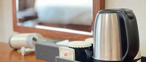 A hotel room with a coffee maker, a hairdryer, and a tissue box on a wooden table.
