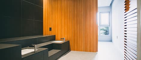A modern bathroom with dark tiles, a wooden accent wall, and a large window providing natural light.