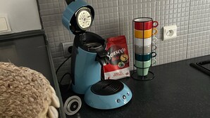 A kitchen with a blue coffee machine, a mug holder with colorful mugs, and a bag of coffee pods. - Joli T2 Climatis? Nimes Proche Gare et Centre Ville (Nîmes)