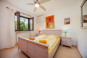 A bedroom with a bed, a nightstand, a lamp, a ceiling fan, a window with curtains, and a wall with a coffee-themed artwork. - Villa "Finca Soliva" with Mountain View, Garden, Wi-Fi, Pool & Terrace (CAPDEPERA)