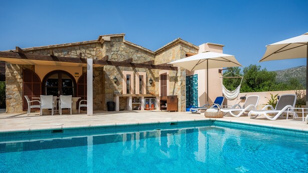 A pool area with lounge chairs, a stone building, and a clear blue sky.