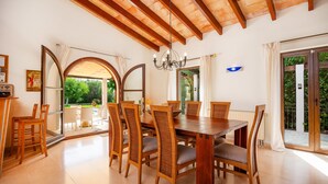 A dining area with a wooden table and chairs, a chandelier, and a view through an arched doorway to an outdoor patio.