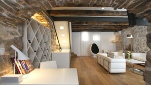 Una sala de estar moderna con pared de piedra, muebles blancos y techo de madera.