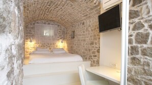 Un dormitorio con pared de piedra, una cama, un escritorio y un televisor montado en la pared.