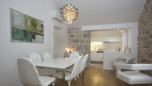 Un comedor moderno con una mesa y sillas blancas, una pared de acento de piedra y una cocina al fondo.