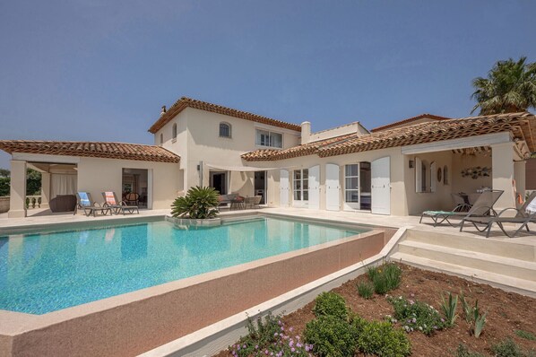 Una villa de dos pisos con piscina, mobiliario de exterior y jardín.