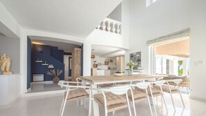 Ein geräumiger Essbereich mit einem Holztisch und weißen Stühlen, im Hintergrund eine Küche und ein Blick ins Freie.