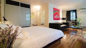 Ein modernes Schlafzimmer mit einem großen Bett, einem Schreibtisch und einem Sessel. Es gibt einen Kleiderschrank und einen Spiegel an der Wand.