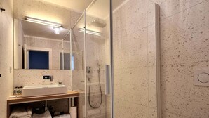 Ein modernes Badezimmer mit einer gläsernen Duschkabine, einem Waschbecken mit Spiegel und einer Toilette.