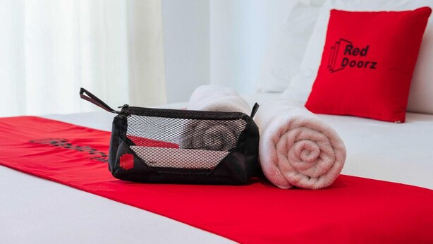 A neatly made bed with a red towel, a black mesh bag, and a red pillow with "Red Doorz" text. - Reddoorz @ Poblacion Sur Sigma (Sigma)