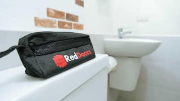 A black bag with "RedDoorz" logo on a white toilet in a bathroom with a sink and brown tiles on the wall.