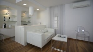 A modern, minimalist living space with a kitchenette, a white sofa, a glass coffee table, and a clear plastic chair. - Deluxe Studio with Balcony 302 Kovačića Street 20 (Split)