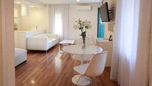 A modern living room with a white sofa, a round dining table with white chairs, a small white table, and a vase with flowers. - Deluxe Studio with Balcony 302 Kovačića Street 20 (Split)