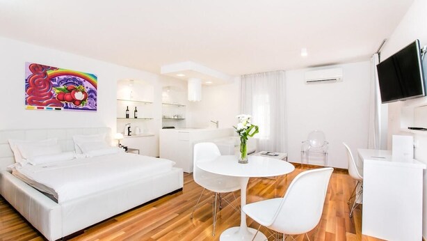 A modern hotel room with a large bed, a dining area with a white table and chairs, a kitchen area, and a TV mounted on the wall. - Deluxe Studio with Balcony 302 Kovačića Street 20 (Split)