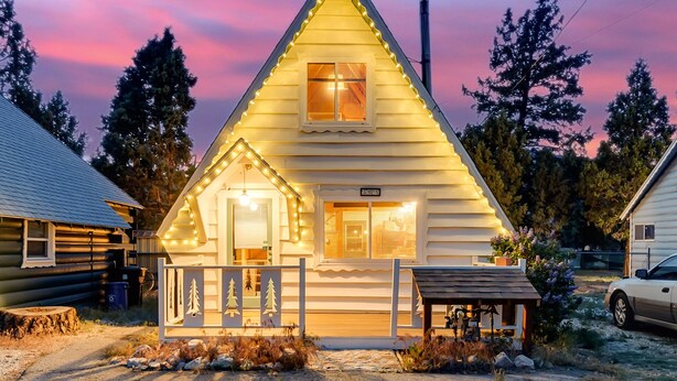 A log cabin with a triangular roof, a porch with a railing, and a small attached shed. - Snow Daze! Visit the mountains! Bring your pup, stay, play & enjoy clean air! (Big Bear)