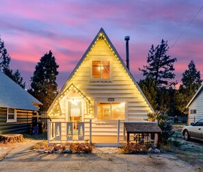 A log cabin with a triangular roof, a porch with a railing, and a small attached shed.