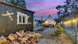 A rustic cabin with a wooden exterior, a pile of firewood, and a small tree. - Snow Daze! Visit the mountains! Bring your pup, stay, play & enjoy clean air! (Big Bear)