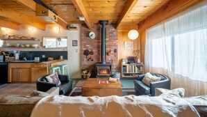 A cozy cabin interior with a kitchen, dining area, and living room, featuring wooden beams, a fireplace, and a large window. - Snow Daze! Visit the mountains! Bring your pup, stay, play & enjoy clean air! (Big Bear)