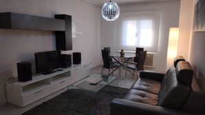 Un salon moderne doté d’un téléviseur à écran plat, d’enceintes, d’une table basse en verre, d’un canapé en cuir et d’un coin repas avec des chaises et une table.