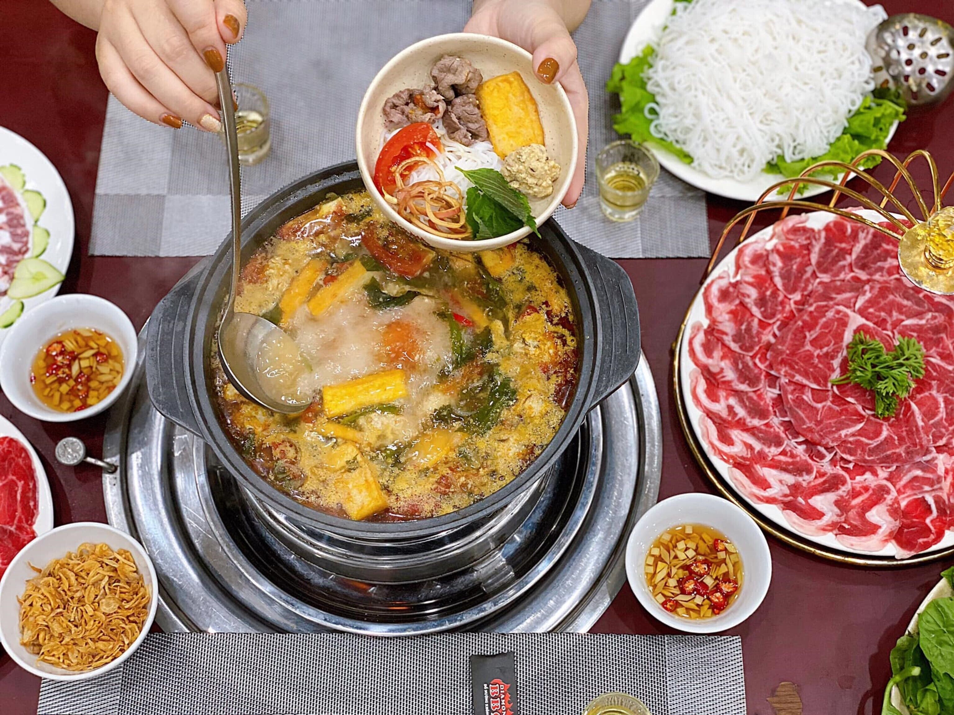 Una olla caliente con diversos ingredientes y un tazón de carne en rodajas.