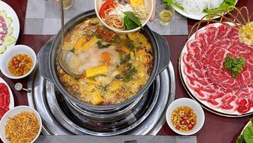 Una olla caliente con diversos ingredientes y un tazón de carne en rodajas.